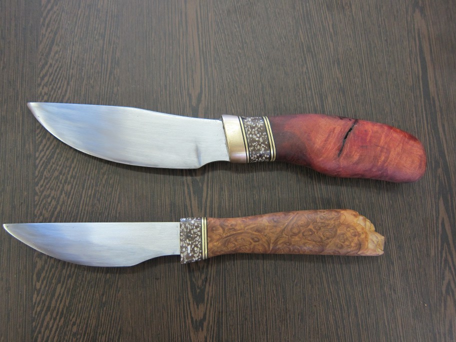 Two finished knives. Layers of brass, plastic visible on one red wood and one other wooden handle.