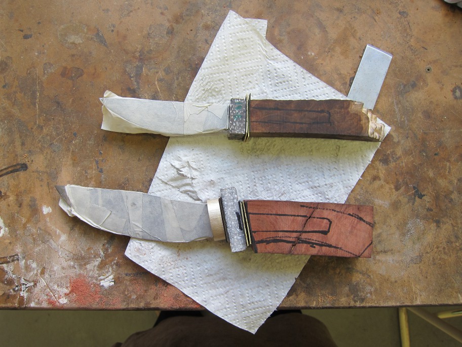 Two knives with rough handles assembled ready for glueing. Layers of brass, plastic visible.