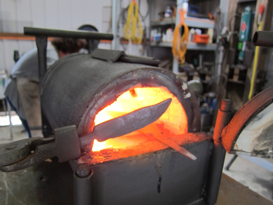 A knife shape is being heated in front of the face of the forge.