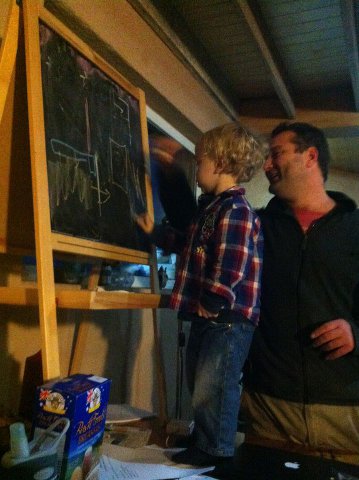 Lucian standing on the table drawning on a chalk board used for teaching the class while Adrian is trying to teach.