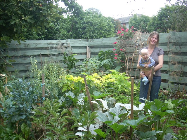 Picture of the lucious Kemp Street Garden with Bryony standing in it holding baby Lucian. Both are smiling